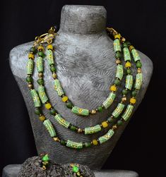 Mesmerizing green layered necklace and matching drop earrings. This stunning set showcases authentic West African beads, expertly crafted into a cascading masterpiece that captures the lush beauty of the region. The multi-strand necklace and elegant earrings blend traditional artistry with contemporary flair, creating a bold statement that's perfect for both everyday wear and special occasions.  Let these pieces' transport you to sun-drenched landscapes and rich cultural heritage. The distance b Green Multi-strand Jewelry For Gift, Artisan Green Jewelry With Unique Variations, Bohemian Green Single Strand Jewelry, Green Bohemian Single Strand Jewelry, Unique Green Jewelry With Polished Beads, Multi-strand Green Jewelry For Gift, Traditional Green Single Strand Jewelry, Green Multi-strand Jewelry Gift, Artisan Green Single Strand Jewelry