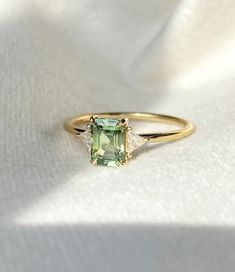 a ring with an emerald colored stone and two diamonds on the side, sitting on a white cloth