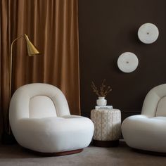 two white chairs sitting next to each other in front of a brown wall with gold accents