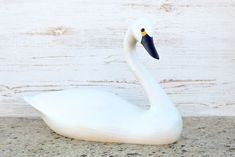 a white swan statue sitting on top of a stone floor next to a wooden wall