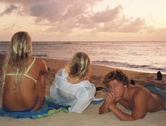 three people are sitting on the beach watching the sun go down in the ocean and one person is covering his mouth