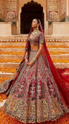 a woman in a red and gold bridal gown standing on steps with flowers all around her