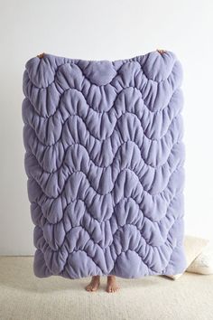 a purple pillow sitting on top of a bed next to a white wall with a person standing in front of it