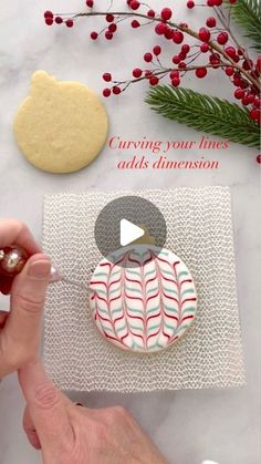 someone is decorating some cookies with red and white stripes on them, while another person holds a cookie in their hand