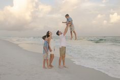 a family playing on the beach with their son in the air and his mother holding him up