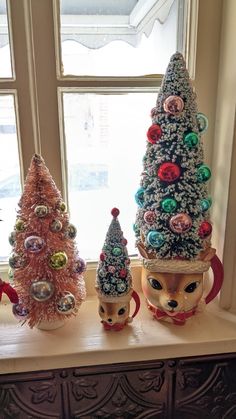 three small christmas trees sitting on top of a window sill next to each other