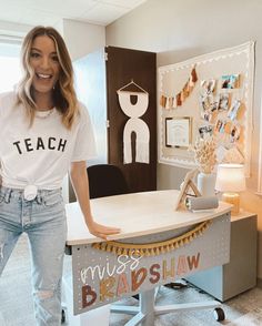 a woman standing in front of a desk with a sign on it that says teach