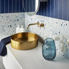 a bathroom sink with a gold bowl and blue tiles on the wall next to it