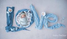 a baby wrapped in blue is laying on the ground next to some flowers and ribbons