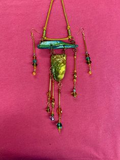 a piece of jewelry is hanging on a pink surface with beads and chains attached to it