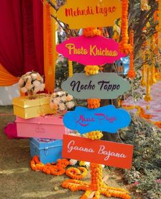 many colorful signs are hanging from a tree in front of some flowers and garlands