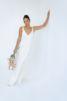 a woman in a white dress holding a bouquet and pointing to the side with her right hand