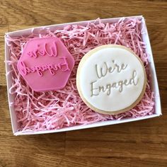 two decorated cookies in a pink box with the words we're engaged on them