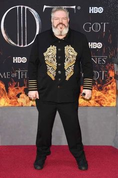 an older man in a black suit and gold jacket standing on a red carpet at the game of thrones premiere