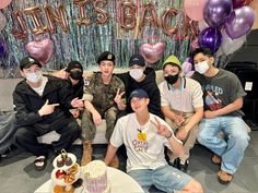 a group of young men sitting next to each other in front of a cake and balloons