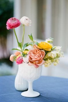 an arrangement of flowers in a white vase on a blue table cloth covered tablecloth