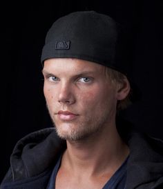 a man with a black hat and blue eyes looks at the camera while wearing a hoodie