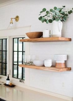 two wooden shelves with bowls and cups on them in a kitchen next to a window