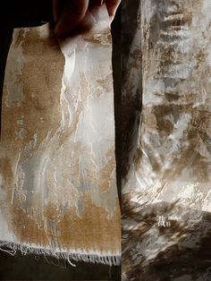 a person holding up a piece of paper with white paint on it and brown foil