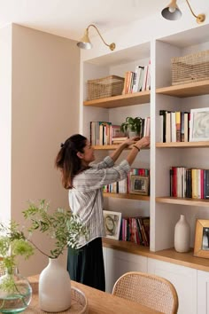 a woman is reaching up to reach the bookshelf in front of her,