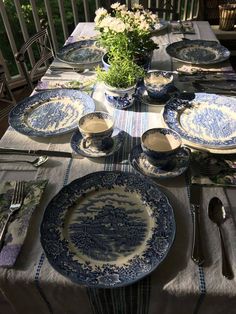 the table is set with blue and white china plates, silverware, and flowers