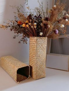 a vase with dried flowers in it sitting on a table next to an empty box