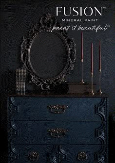 a black dresser with candles and a mirror on it's top, in front of a dark wall