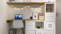 a desk with a laptop computer on top of it next to white cabinets and drawers