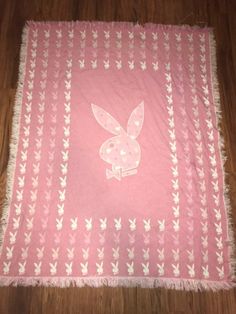 a pink and white blanket with an image of a rabbit on the front, sitting on top of a wooden floor