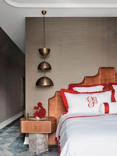 a bed with white and red sheets in a bedroom next to a wall mounted lamp