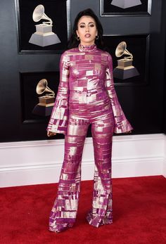 a woman in purple and gold outfit standing on red carpet with her hands behind her back