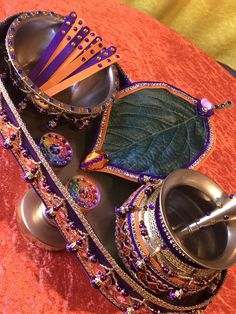 an assortment of jewelry sits on top of a red table with a green leaf in the middle