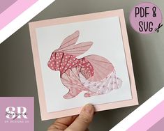 a hand holding up a pink and white card with a rabbit on it's back