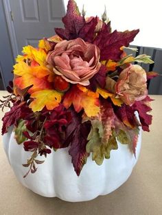 a white pumpkin filled with lots of different colored leaves and flowers sitting on top of a table