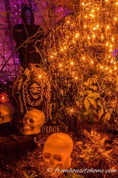 halloween decorations with lights and fake skulls on the ground in front of a tree filled with pumpkins