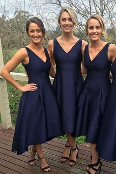 three beautiful women standing next to each other on a wooden deck wearing dresses with straps