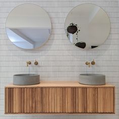 two round mirrors are on top of a wooden cabinet in front of a white tiled wall