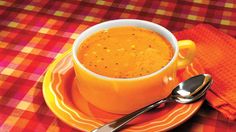 a bowl of soup on a plate with a spoon and orange napkin next to it