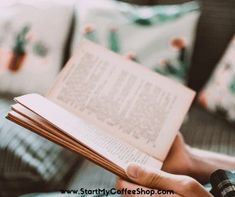 a person sitting on a couch holding an open book in their hands and reading it