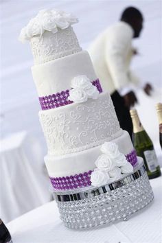 the wedding cake is decorated with white flowers and purple ribbon, while the groom stands behind it