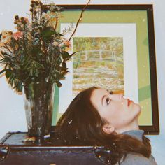 a woman is looking up at a vase with flowers in it and a painting on the wall behind her