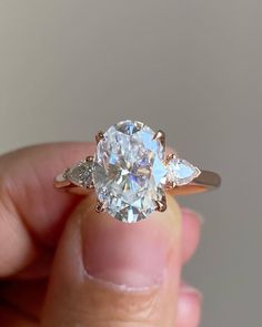 a person holding an engagement ring with three pear shaped diamonds on the band and side stones