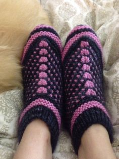 a person's feet wearing knitted slippers on top of a bed next to a cat