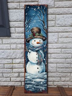 a snowman standing in front of a brick wall with a painting on it's side