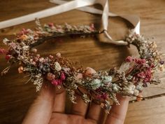 a hand holding a flower crown on top of a wooden table