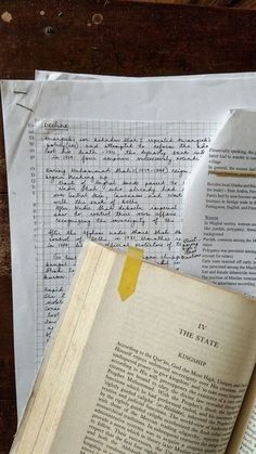 an open book sitting on top of a wooden table next to papers with writing on them