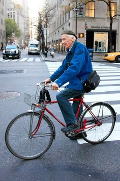 an old man is riding his bike down the street in the middle of the city