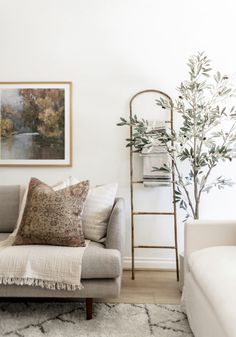 a living room with a couch, chair and tree in the corner next to it