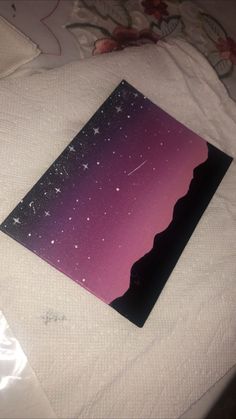 a purple and black card with stars on it sitting on a white bed sheet next to a pillow