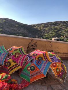 several colorful umbrellas laying on the ground in front of some hills and buildings with trees